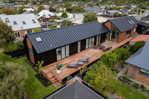 Drone view of a contemporary black and timber home with large outdoor deck and landscaped gardens