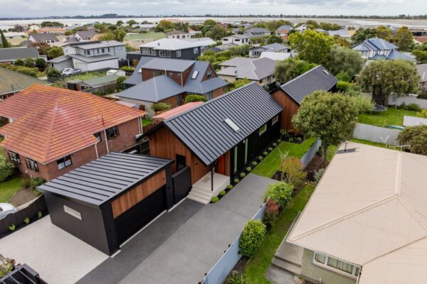 Drone view of a contemporary home with black garage, concrete driveway and landscaped garden