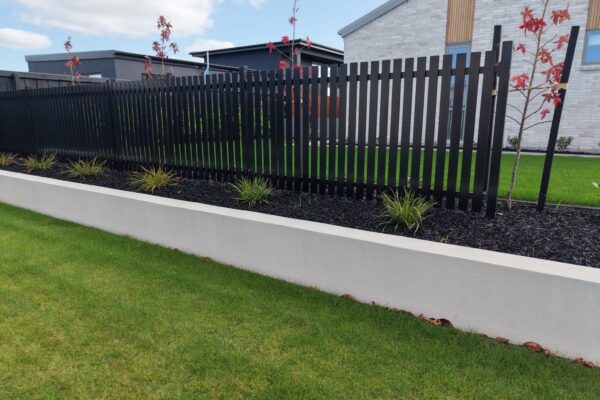 Black vertical slat fence above a rendered garden wall with fresh planting and lawn