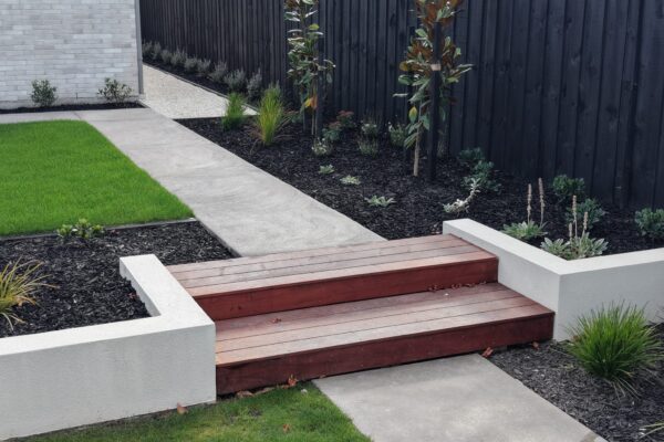 Timber garden steps connecting concrete paths through black mulch planting beds