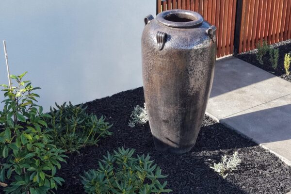 Large feature urn in a landscaped garden bed with black mulch and low planting