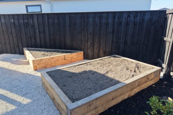 Raised timber garden beds with white chip path and black boundary fence