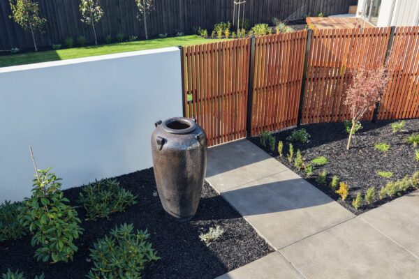 Feature urn beside concrete paving, timber gate and newly planted garden beds