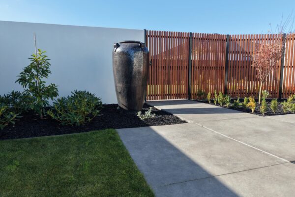 Contemporary garden with feature urn, timber screen fencing, lawn and concrete paving